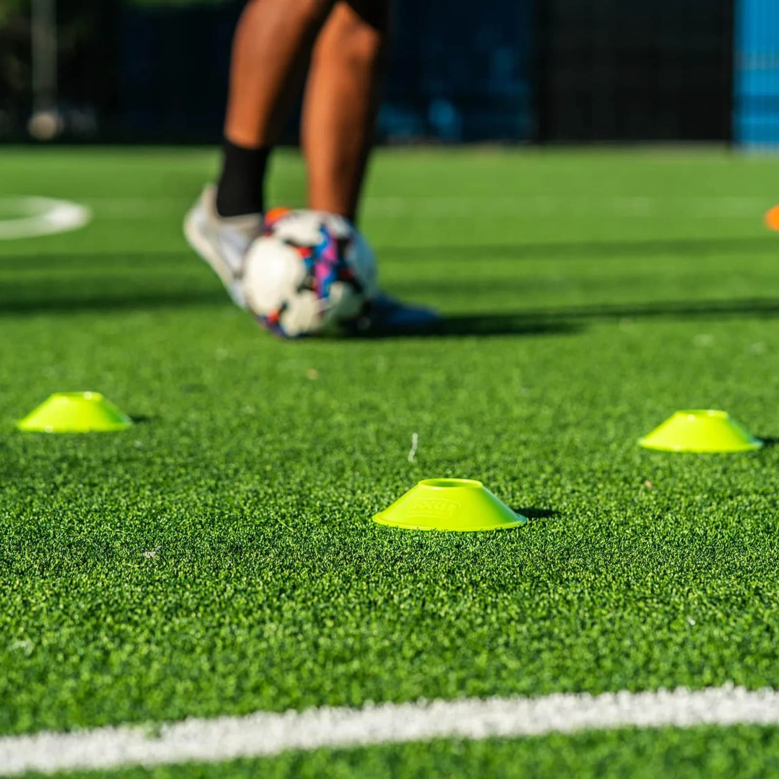 Player dribbling a soccer ball through cones during a daytime training drill